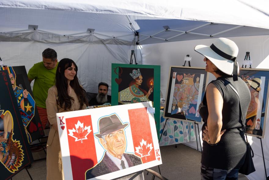 Art fair booth with people browsing colorful paintings displayed on easels.