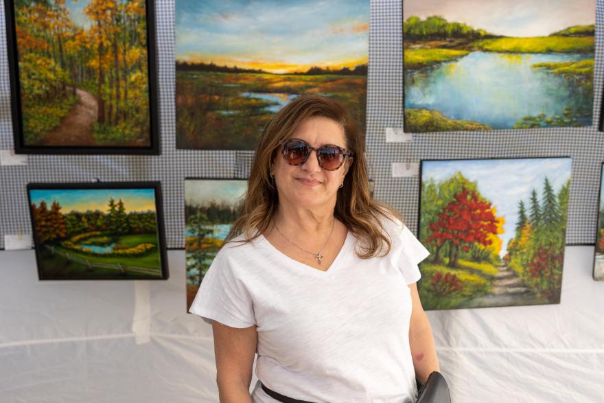 Woman in sunglasses in front of landscape paintings.