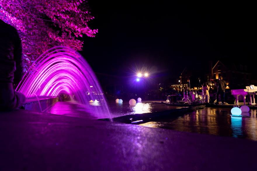 Fountain at night with vibrant pink and purple lighting.