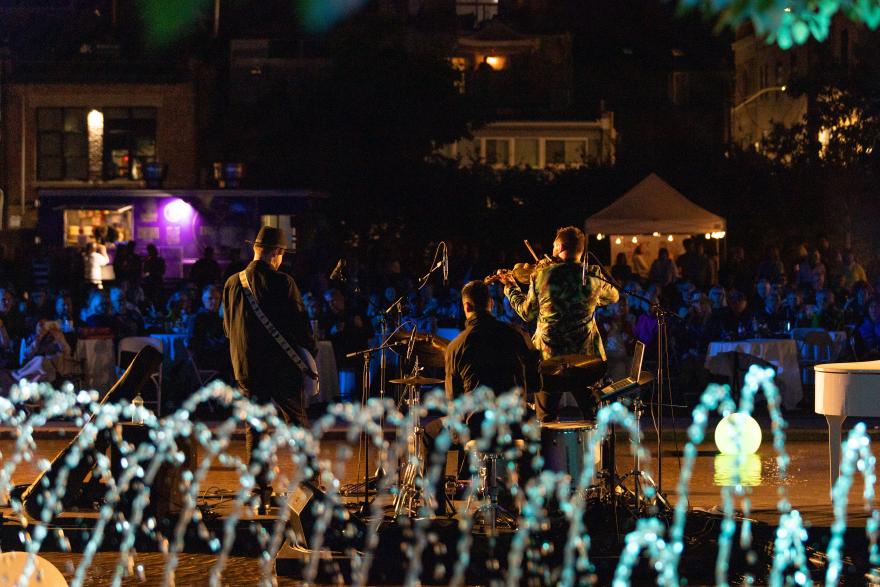 Band performing at night in front of a fountain with an audience.