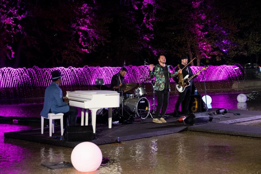 Jazz band performing by a fountain, illuminated by purple lights.