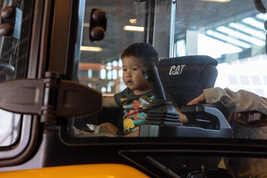 Toddler sitting inside a construction vehicle, looking out the window.