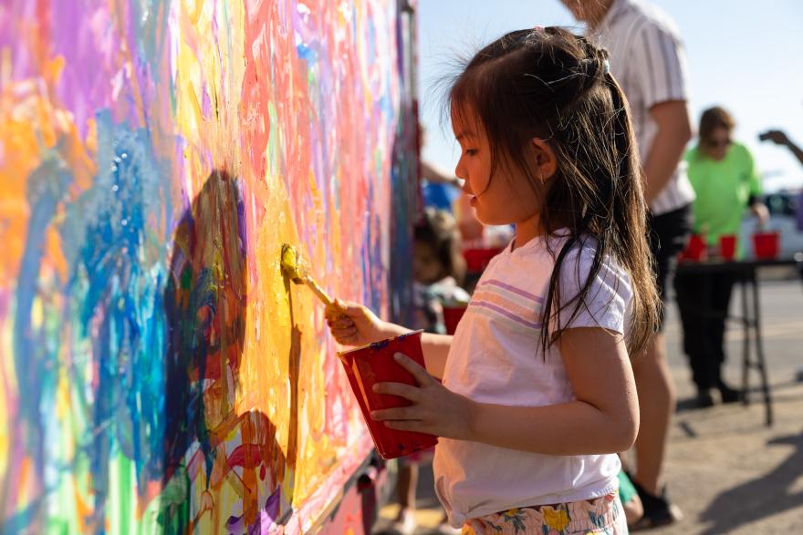 Child painting on a colorful outdoor mural in sunlight.