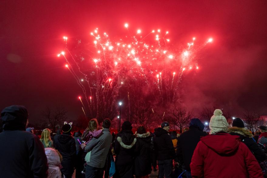 Crowd watching vibrant red fireworks in the night sky.