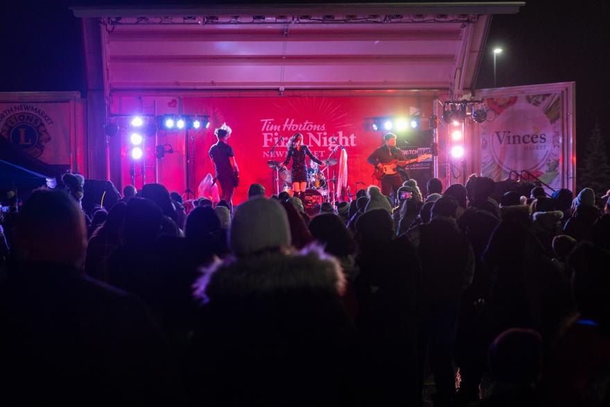 Crowd watching a band perform on a stage with colorful lights at night.