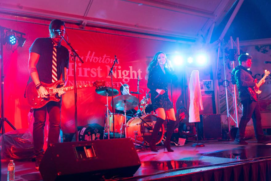 Band performing on stage with red lighting and colorful spotlights.