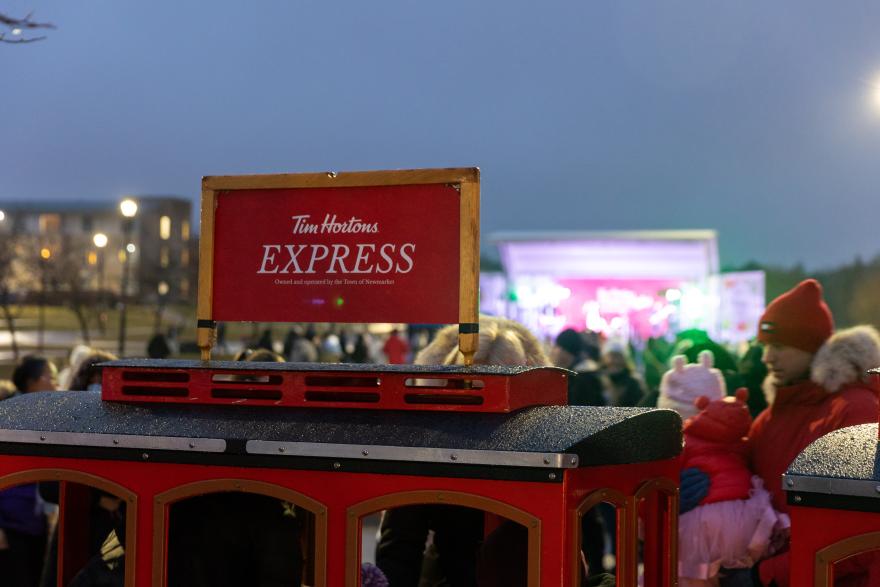Red trolley in festive outdoor event with crowd nearby.