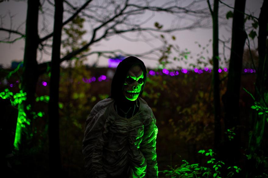 Eerie figure in a forest, face glowing green, with purple lights in the background.