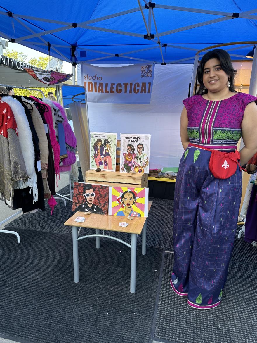 Woman in vibrant outfit at outdoor market stall with artwork on display.