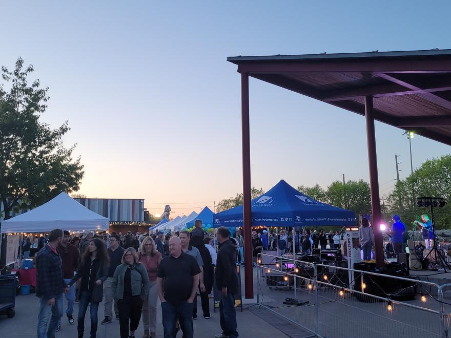 People enjoy a lively outdoor festival at dusk with tents and lights.