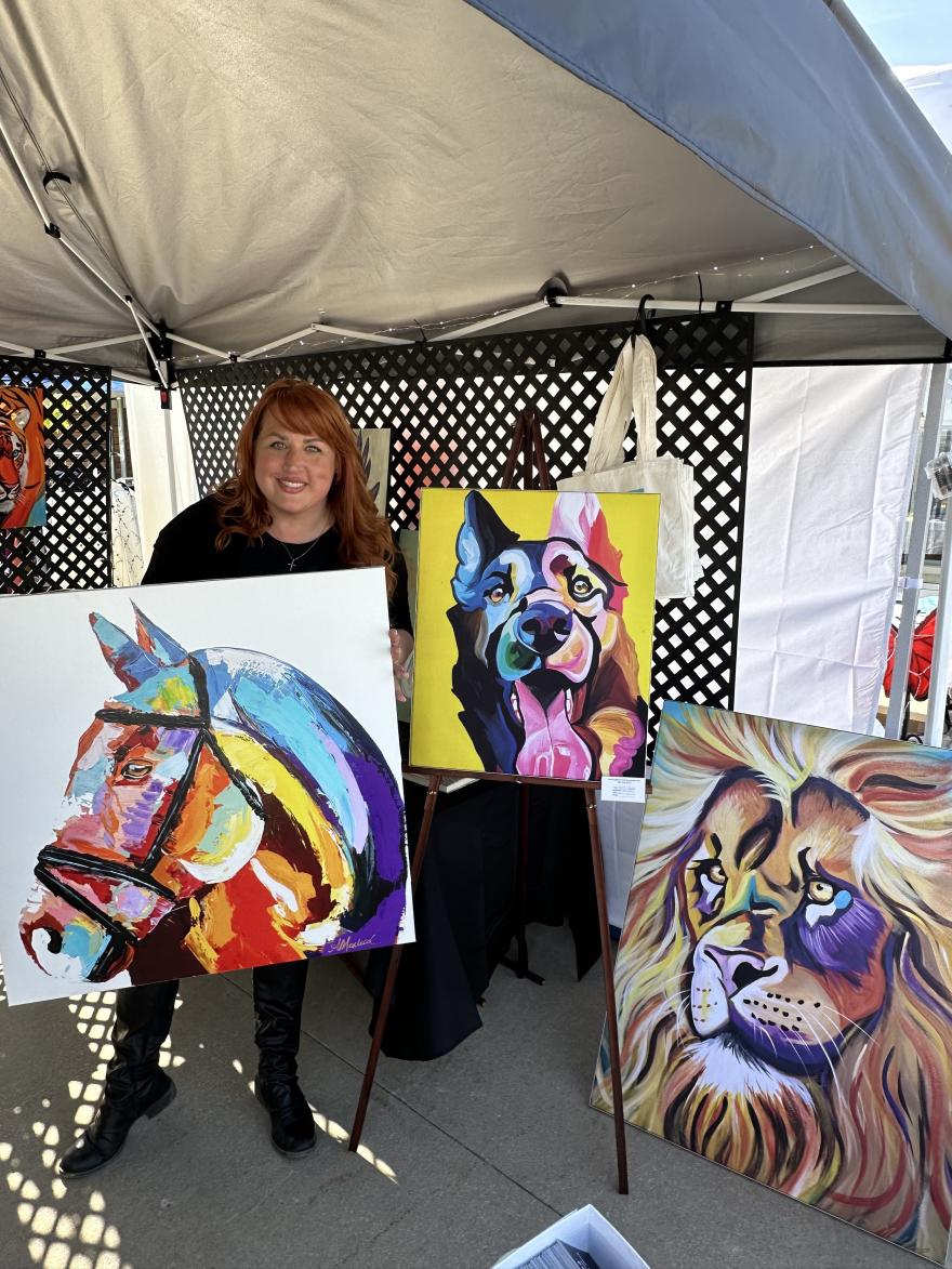 Artist with colorful animal paintings under a canopy.