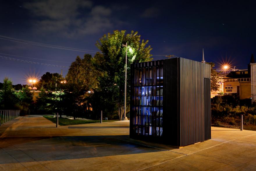 Night scene with a black, cube-shaped structure (Story Pod) near a lit path and trees.