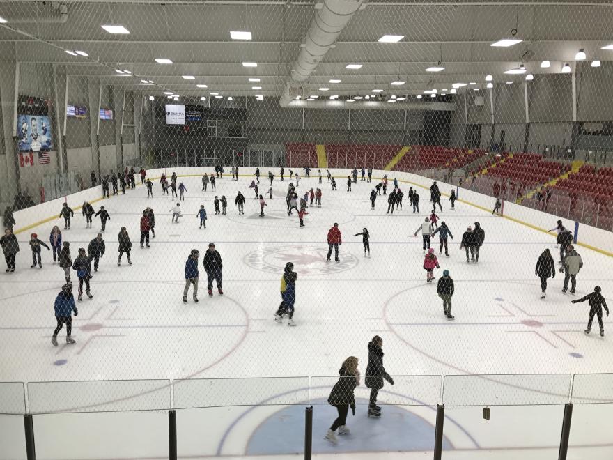Ice rink with people skating, red seats, and bright overhead lights.