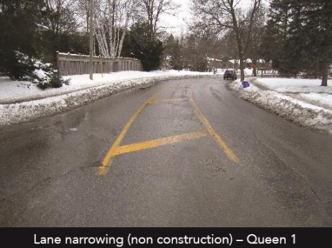 Road with yellow lane narrowing lines, snowy sides, trees ahead.