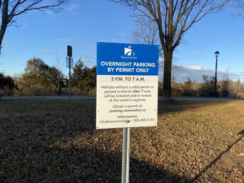 Blue parking sign in a park with trees and a path in the background.