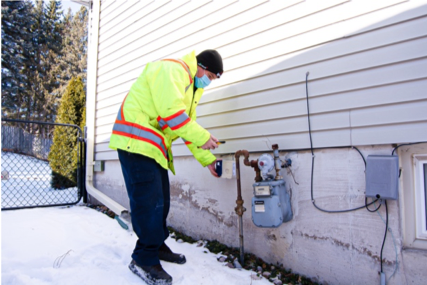 Worker in a bright jacket inspecting a gas meter in a snowy yard.