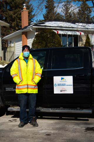 Worker in a yellow jacket stands by a black truck in a snowy driveway.