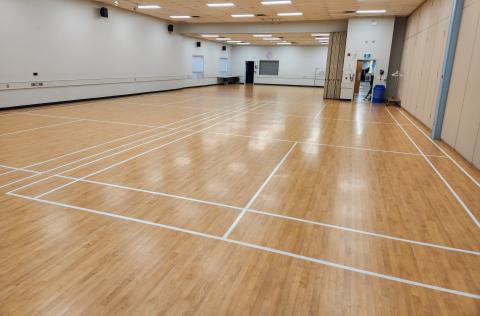 Large empty gymnasium with wooden floor and white lines. Bright overhead lights.