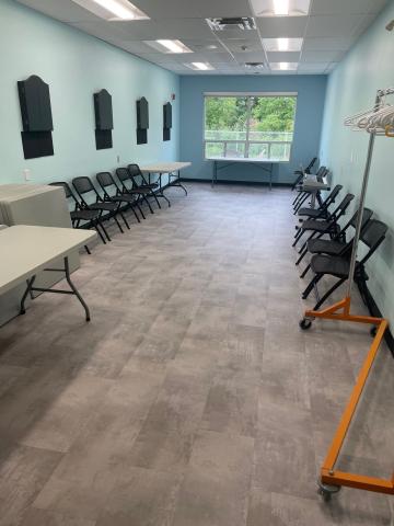 Empty room with folding chairs and tables, pale blue walls, large window.