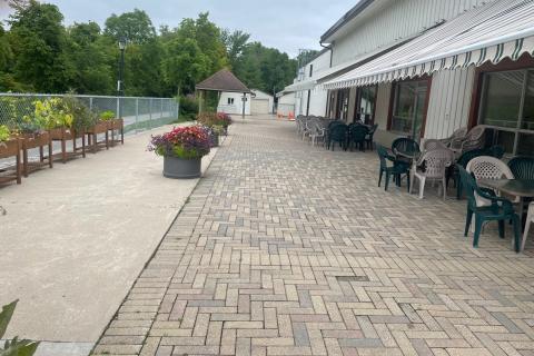 Paved patio with tables, chairs, plants, and a canopy, adjacent to a garden walkway.