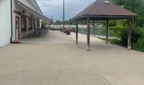 Wide concrete path by a building and gazebo, cloudy sky above.