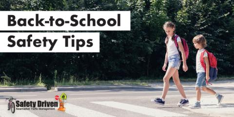 Two children with backpacks crossing a street at a crosswalk.