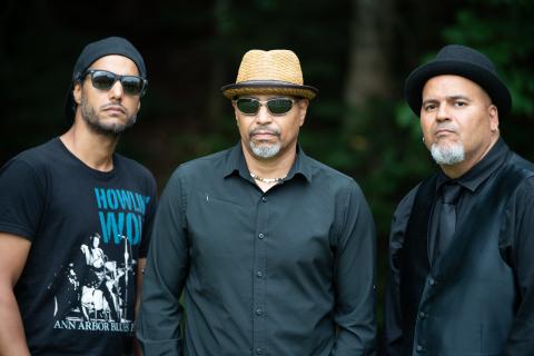 Three men in hats and sunglasses, outdoors, with serious expressions.