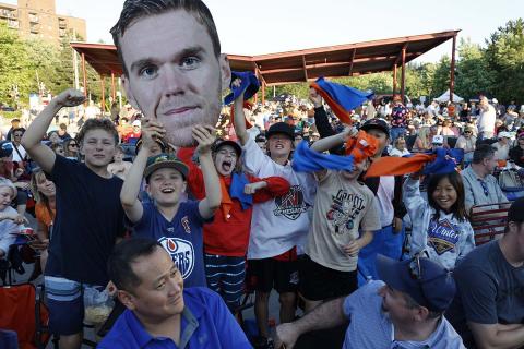 Crowd of enthusiastic fans holding a large face cutout at an outdoor event.