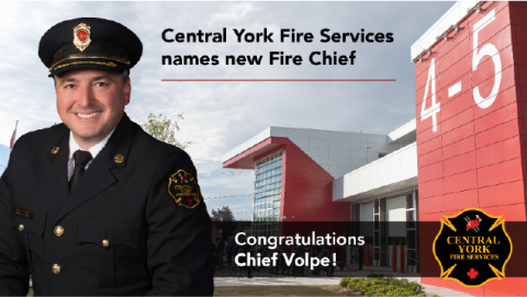 Fire chief in uniform stands in front of a red and white building.