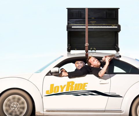 Car with two men and a piano strapped on the roof.