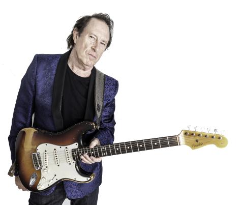 Man in a blue jacket holds an electric guitar against a plain background.