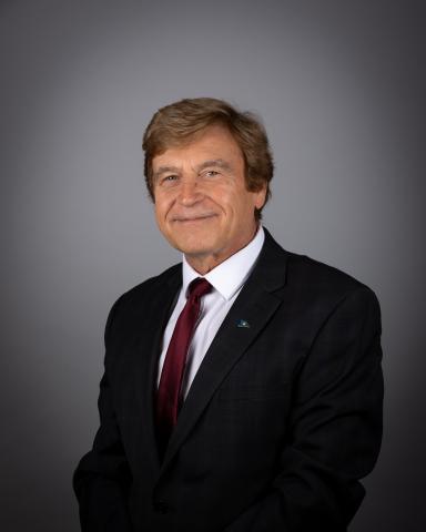 Tom Vegh in a dark suit and red tie against a gray background.