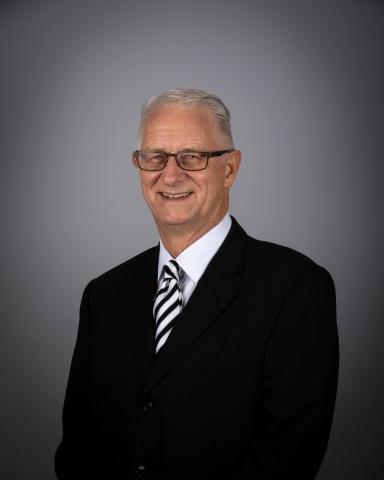 Victor Woodhouse in a suit with glasses, smiling against a gray background.