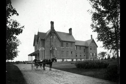Black and white photo of historic house with horse and carriage in foreground
