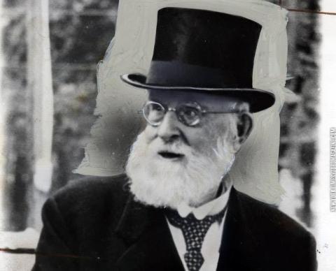 Historic black-and-white portrait of Sir William Mulock wearing a tall top hat, round eyeglasses, a dark suit, and a patterned tie.