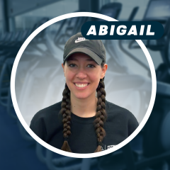 Smiling woman with braided hair and a cap in a gym setting.
