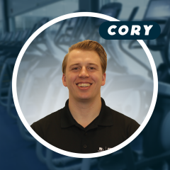 Smiling man in black shirt against blurred gym background.