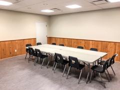 Conference room with a long table and ten chairs, beige walls and wood paneling.