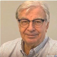 Elderly man with glasses, wearing a striped shirt, smiling slightly.
