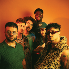 Group of six people posing with colorful and stylish outfits against an orange background.