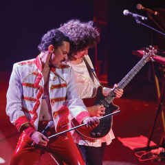 Two musicians perform energetically on stage, one playing guitar.