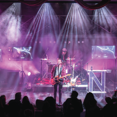 Rock band performing on stage with colorful lights and silhouettes of an audience.