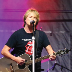 Singer with guitar performs under purple lighting.