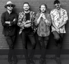 Four men standing against a brick wall, smiling casually.