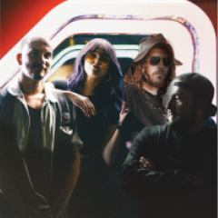 Group of four people posing under neon lights, one wearing sunglasses and a hat.