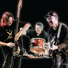 Rock band performing energetically on stage with guitars and drums.