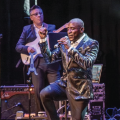 Singer performing on stage with a guitarist, under dramatic lighting.