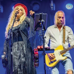 Singers performing on stage, a woman in a red hat and a man with a yellow guitar.