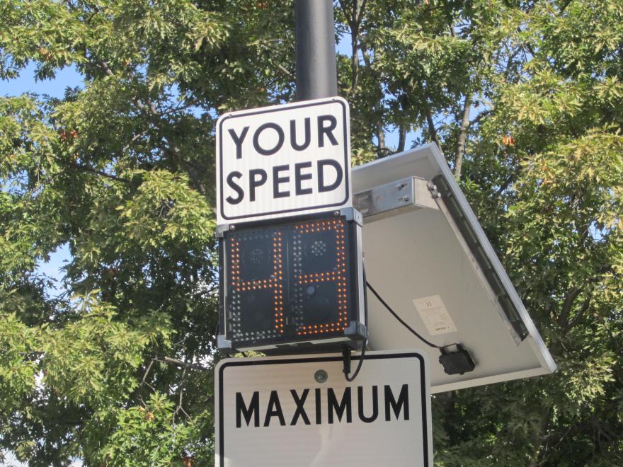 Speed limit sign with digital display under trees.