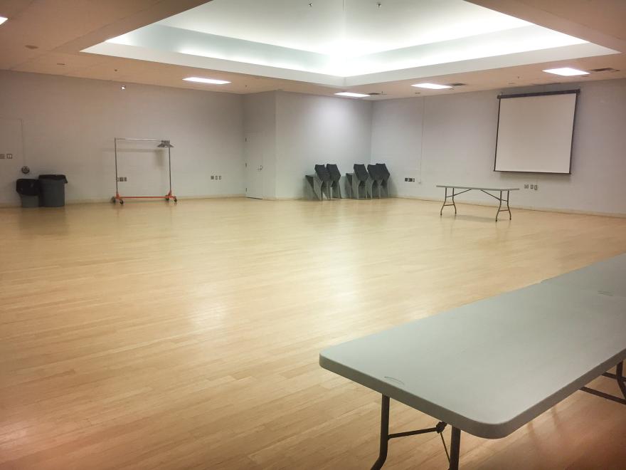Large empty room with tables, chairs stacked, and a projection screen.